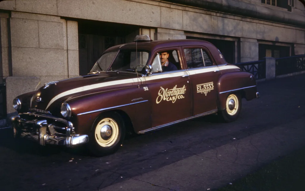 A maroon Northgate Cab Co sedan at the kerb in Seattle with its driver at the wheel, the company name and telephone number painted on the door.